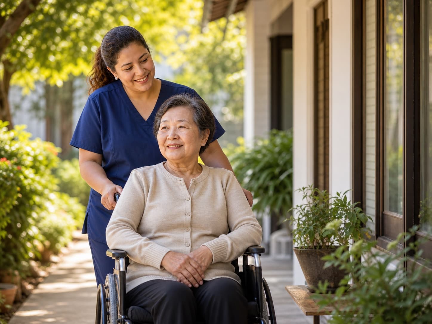 Hispanic caregiver in care attire supporting an older Chinese woman in a wheelchair