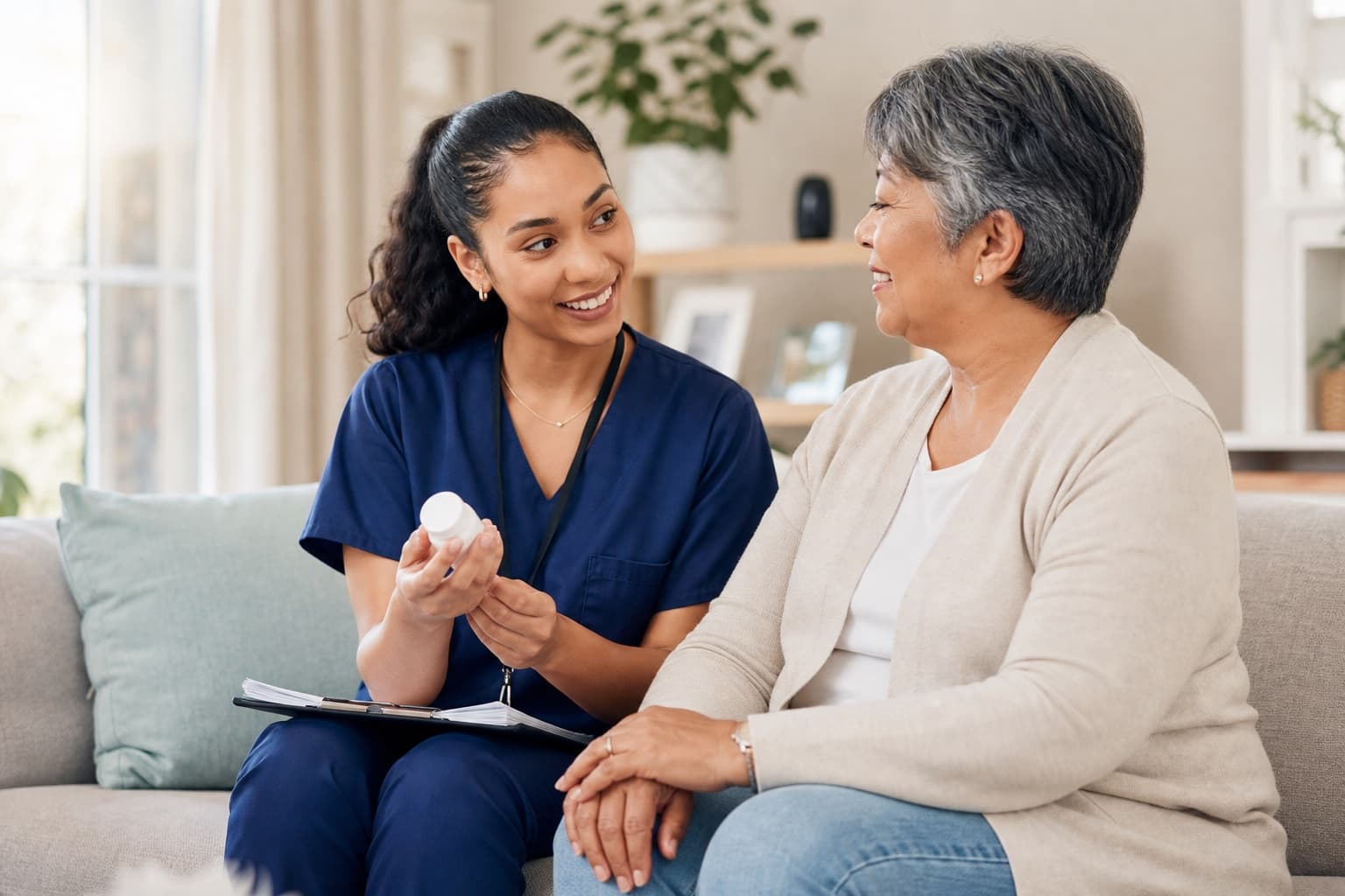 Home-health professional discussing medication support with an older adult in a bright living room
